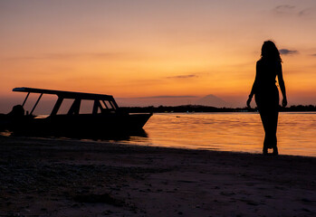 Silhouette of woman against tropical sunset at the beach by the fishing boat at the ocean