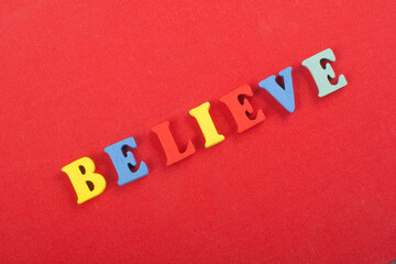BELIEVE word on red background composed from colorful abc alphabet block wooden letters, copy space for ad text. Learning english concept.