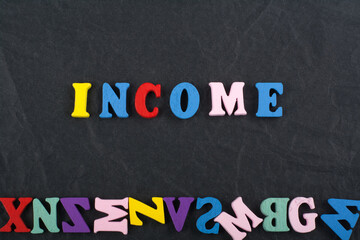 INCOME word on black board background composed from colorful abc alphabet block wooden letters, copy space for ad text. Learning english concept.