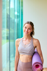 Portrait Of Woman Wearing Gym Clothing At Gym Or Yoga Studio Holding Exercise Mat