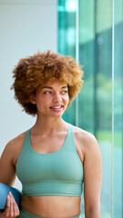 Portrait Of Woman Wearing Gym Clothing At Gym Or Yoga Studio Holding Exercise Mat
