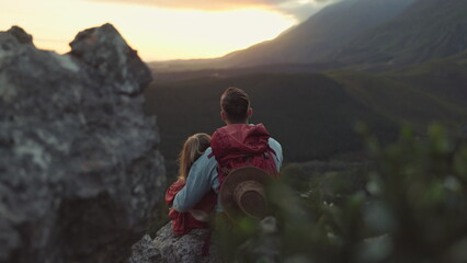 Hiking, mountain and sunrise, couple relax on outdoor adventure and peace in nature with romance from back. Trekking, rock climbing and love, man and woman with sunset horizon view on cliff together.