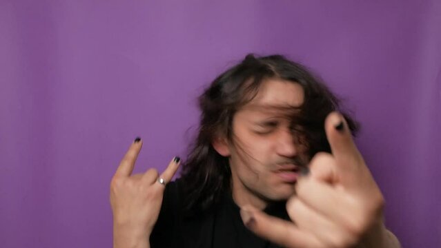 Young handsome punk guy shakes his long hair and shows the goat sign. 