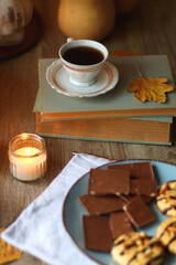 Cup of tea or coffee, plate with desserts, dried oranges, bowl of grapes, scented candles, vintage books, pumpkins and autumn leaves on the table. Autumnal hygge. Selective focus.