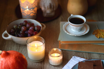 Cup of tea or coffee, plate with desserts, dried oranges, bowl of grapes, scented candles, vintage books, pumpkins and autumn leaves on the table. Autumnal hygge. Selective focus.