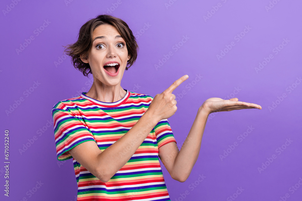 Sticker Photo of astonished cute cheerful person direct finger hand hold empty space isolated on violet color background