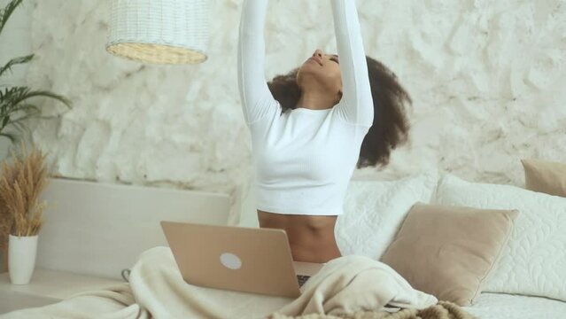 Positive tired curly young woman feels satisfied with distance remote work well done at home Calm self employee female relax after hard working day finished project on laptop computer indoors