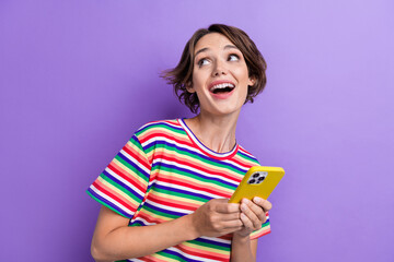 Portrait of pretty cheerful girl hold smart phone look empty space ad isolated on purple color background