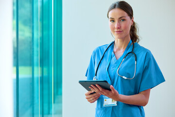 Portrait Of Female Doctor With Serious Expression Wearing Scrubs With Digital Tablet In Hospital