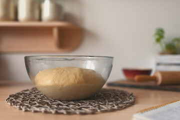 A table on which lies the leavened dough with yeast in a glass bowl, wooden rolling pin and a recipe book.