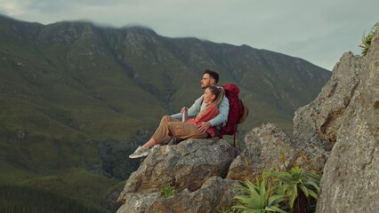 Hiking, mountain and view, couple relax on outdoor adventure travel and peace in nature with romance. Trekking, rock climbing and love, man and woman in natural environment sitting on cliff together.