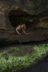 Sexy girl in green underwear posing against the background of rocks smeared with volcanic sand