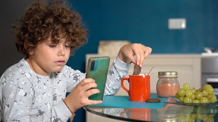 9 year old boy have a breakfast at home looking at the smart phone - addiction to social networks...