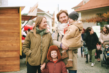   Outdoor portrait of happy family of four, young couple with 2 little children, cold weather, fall time - obrazy, fototapety, plakaty