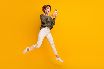 Photo of crazy funky cheerful girl wear trendy clothes walking empty space reading social media isolated on yellow color background