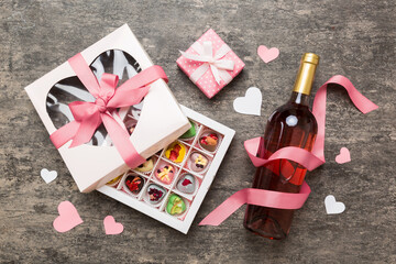 Bottle of red wine on colored background for Valentine Day with gift and chocolate. Heart shaped with gift box of chocolates top view with copy space
