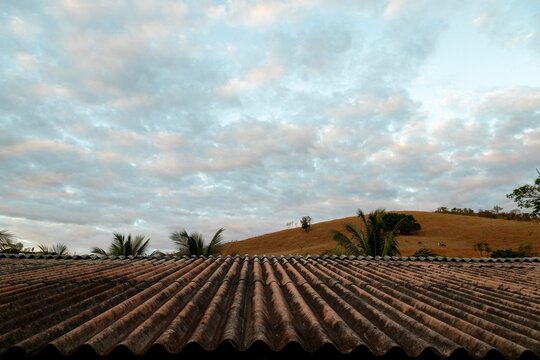 Telhado de telha de amianto ao fundo serra e céu azul. 