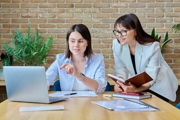 Two serious business women working in office, typing on laptop