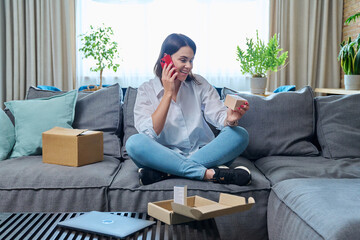 Young happy woman talking on mobile phone, sitting at home, unpacking box