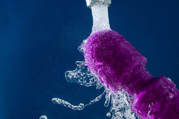 Purple vibrator under running water on a blue background. waterproof sex toy. 