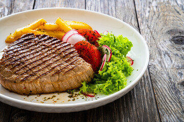 Grilled beef steak with fresh vegetable salad and French fries on wooden table
