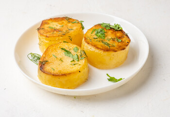 Potato fondant in a white plate sprinkled with herbs, light table.