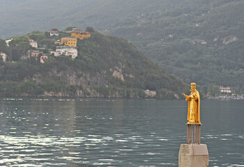 Golden statue of Saint Nicholas, the patron saint, in Lake Como in Lecco, indicating the water level. Mountains in the background, selective focus