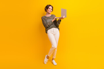 Full length photo of adorable cute girl dressed stylish clothes use wireless gadget netbook isolated on yellow color background