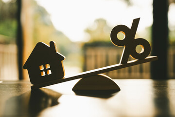 Wooden house model, Percentage symbol on wooden balance with sunlight, Concepts of interest, a symbol for buying a new house, property insurance and security, affordable housing concepts.