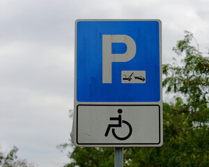 Close-up photo of a handicapped parking sign attached to a pole with a tree in the background and sky in the background