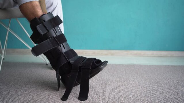 Man putting on ankle brace, Orthopedic ankle support shoes. Injuried guy on chair with Splint, walker boot, Orthosis. Ankle Orthosis