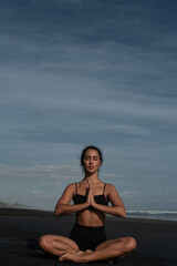 Naklejka na ściany i meble Beautiful girl doing yoga on a black beach near the ocean
