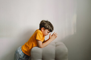 A boy in an orange T-shirt prays at home. Reading the Holy Bible. Concept for faith, spirituality and religion. Peace, hope.
