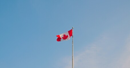Fototapeta premium National flag of Canada also known as The Maple Leaf. Red white flag of Canada fluttering in breeze. Slow motion bottom view of Canadian flag high in sky. Enjoy atmosphere of Canada and Canadian life