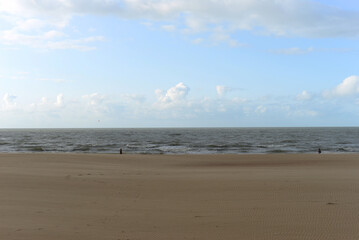 Two unrecognizable persons in the distance on deserted Ostend beach at the North Sea on an autumn day in October with blue sky and fluffy clouds