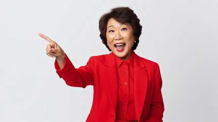 Surprised senior asian lady pointing upper left corner, checking out promo offer and smiling amazed, standing in red blazer over white background - obrazy, fototapety, plakaty