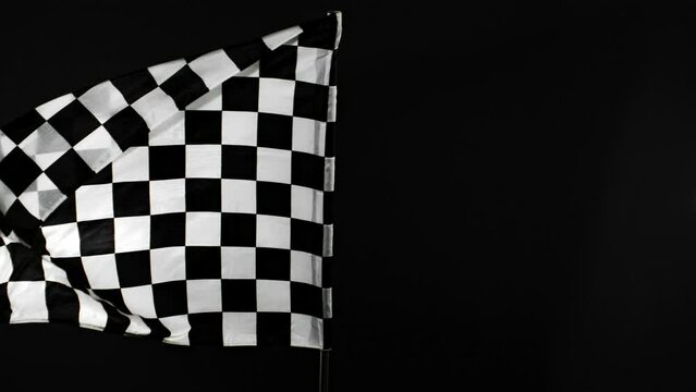 Super Slow Motion of Checkered Race Flag Waving Continuously in the Wind, 1000fps. Formula Racing Flag Isolated on Black Background. Victory, Achievement, Success and Sport Concept. Speed Ramp Effect.
