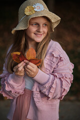 Portrait of a smiling girl dressed in an autumn trendy fashion style with autumn fallen leaves in her hand isolated on an nature background.