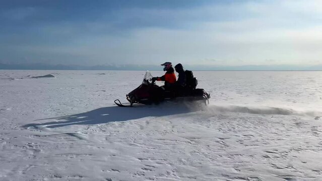 A man in a red jacket on a snowmobile quickly rides along the winter snowy Lake Baikal at high speed