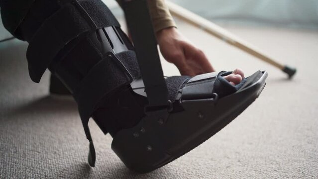 Young man with leg injury using Splint, walker boot, Orthosis. Guy with sprained ankle at home