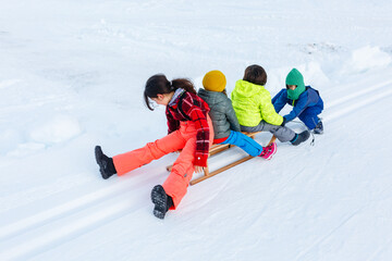 group of children riding one wooden sled down snow slope playing together