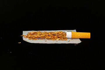 An open filtered cigarette on a on a rolling paper with the tobacco exposed and scattered. Very...