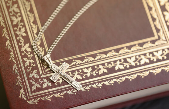 Silver necklace with crucifix cross on christian holy bible book on black wooden table. Asking blessings from God with the power of holiness, which brings luck and shows forgiveness.