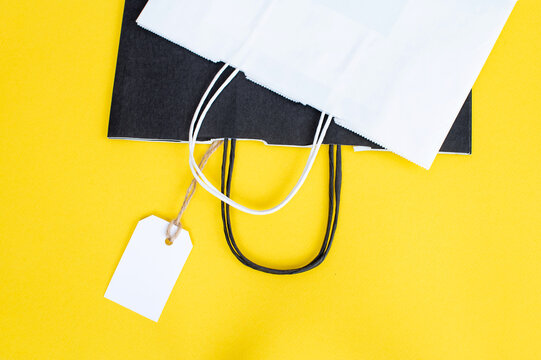 White blank tag with paper black and white recyclable bag on yellow background. Paper bag handles.