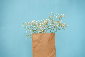 Craft packaging with small white gypsophila flowers on a blue background. Place for the logo