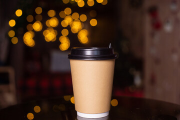 A disposable coffee cup with a lid on the background of a Christmas tree. Place for advertising