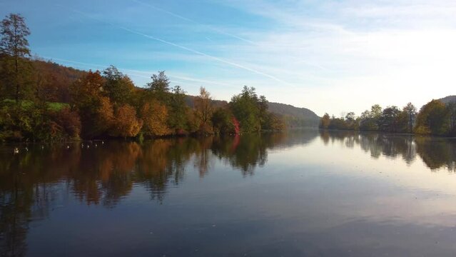 Drone flying low over river between colorful autumn leaf tree forest on sunny day_2