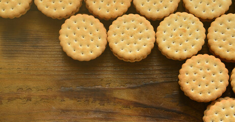A round sandwich cookie with coconut filling lies in large quantities on a brown wooden surface. Photo of edible treats on a wooden background with copy space