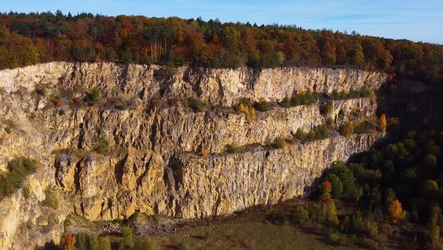 Drone flying sideways over abandoned quarry in autumn with colorful lead tree foliage
