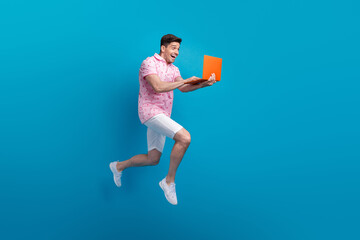 Full length profile photo of impressed cheerful man jump run use netbook empty space isolated on blue color background